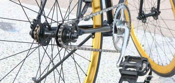 Nahaufnahme eines gelben Fahrrads, zusehen ist der untere Teil eines Fahrrads mit den Pedalen und der Kette. 