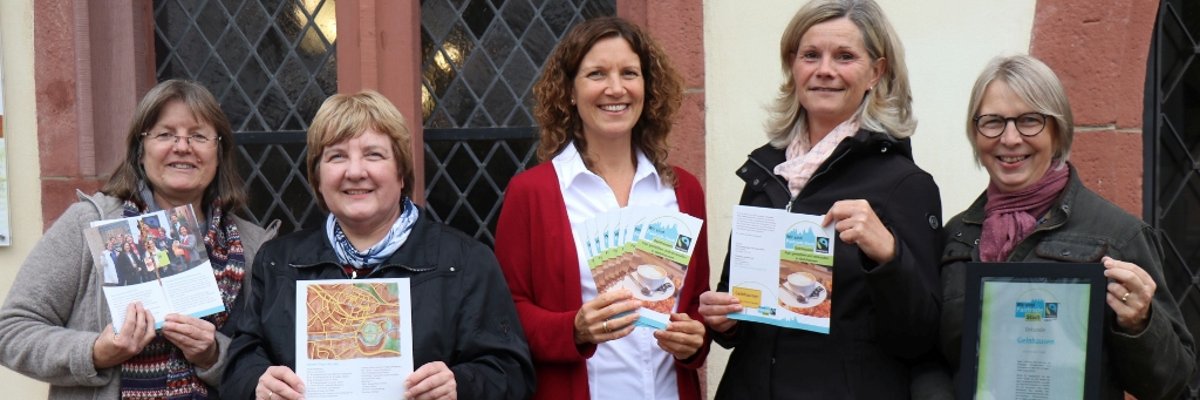 Auf dem Bild sind 5 Mitarbeiter der Stadterwaltung Gelnhausen zu sehen. Diese stehen vor dem Rathaus und halten alle Zertifikate und Flyer für Fairtrade Programme vor sich. 