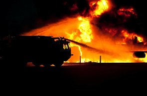 Feuer wird gelöscht Das Bild zeigt einen Großbrand der von einem Feuerwehrfahrzeug gelöscht wird. Es ist nur die Silhouette des Feuerwehrfahrzeuges zusehen.