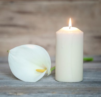 Eine weiße Calla-Blüte neben einer weißen brennenden Kerze.