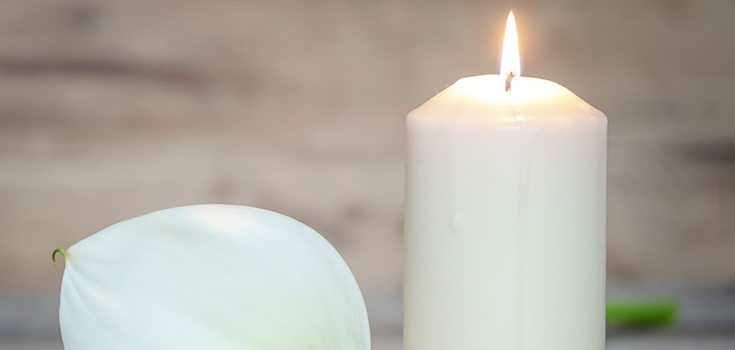 Eine weiße Calla-Blüte neben einer weißen brennenden Kerze.