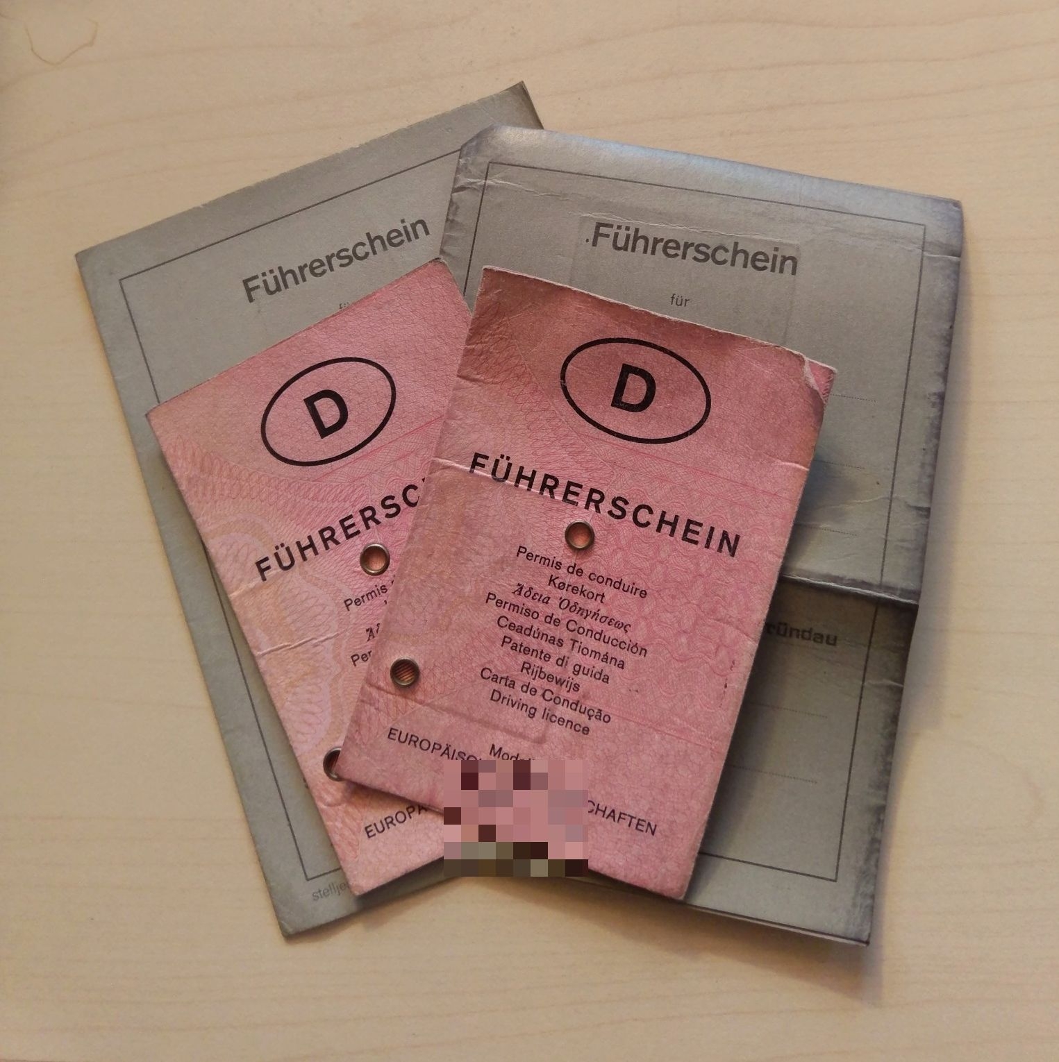 Zu sehen sind zwei zusammengefaltete Führerscheine, die auf einem Tisch liegen. An den Führerscheien sind rosa Zettel befestigt auf dehnen Führerschein steht.