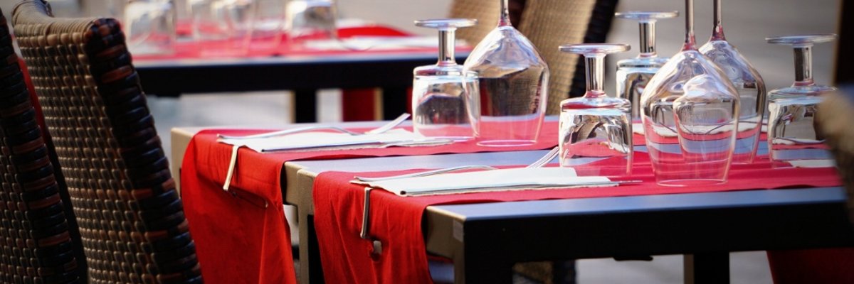 Zu sehen sind zwei Tische mit jeweils vier Stühlen. Auf den Tischen befinden sich jeweils zwei rote Tischläufer und mehrere umgedrehte grläser. 