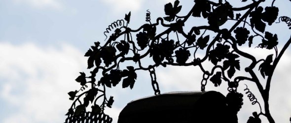 Zu sehen ist die Silhouette eines Schildes, das an einer Hauswand befestigt ist. Im Hintergrund sieht man einen bewölkten Himmel. 