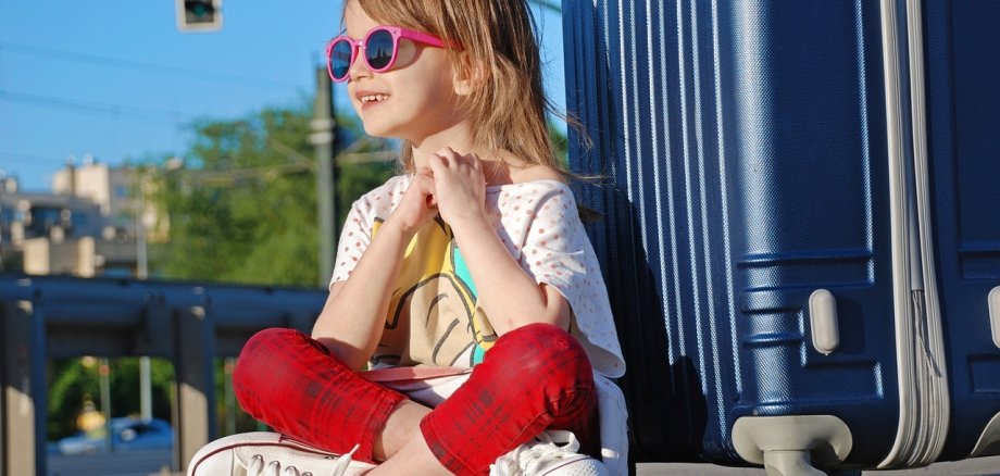 Ein Kind sitzt vor einem Rollkoffer.