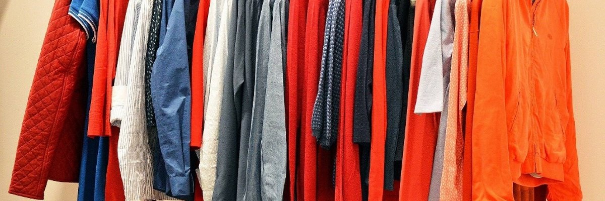 Symbolbild zeigt eine Kleiderstange, an der diverse Oberbekleidungsstücke in verschiedenen Farben hängen.