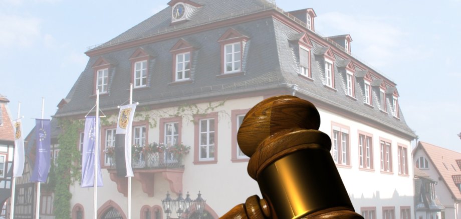 Schiedsamt Symbolbild mit einem überdimensionalen Richterhammer im Vordergrund, das Rathaus im Hintergrund.