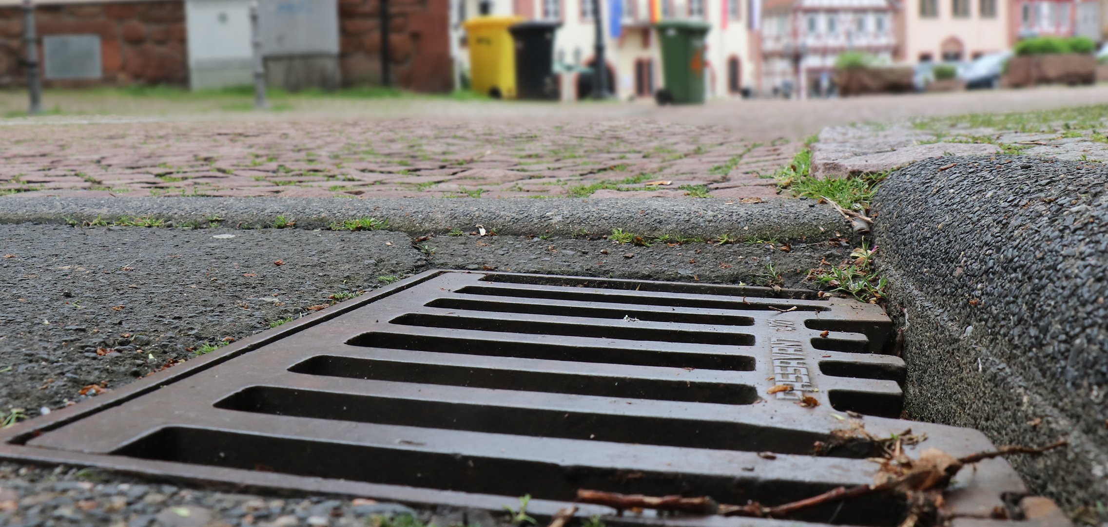 Nahaufnahme eines Straßenablaufs, im Hintergrund Obermarkt und Rathaus.