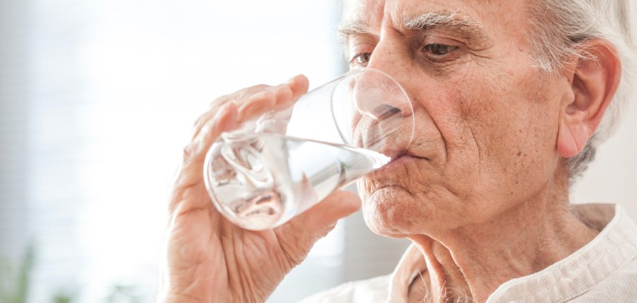 Hitzeschutz Senioren Ein älterer Mann trinkt aus einem Wasserglas.