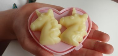 Mitmachmuseum für Kinder Man sieht eine offene Hand, auf der ein herzförmiger Teller liegt worauf zwei gelbe Einhornköpfe aus Seife liegen.