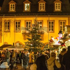 Der Weihnachtsmarkt ist bei Nacht im vollen Gange, im Hintergrund steht das Rathausgebäude 