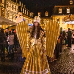 Eine Frau verkleidet als Engel mit einem Goldenen Gewand steht auf dem Weihnachtsmarkt 