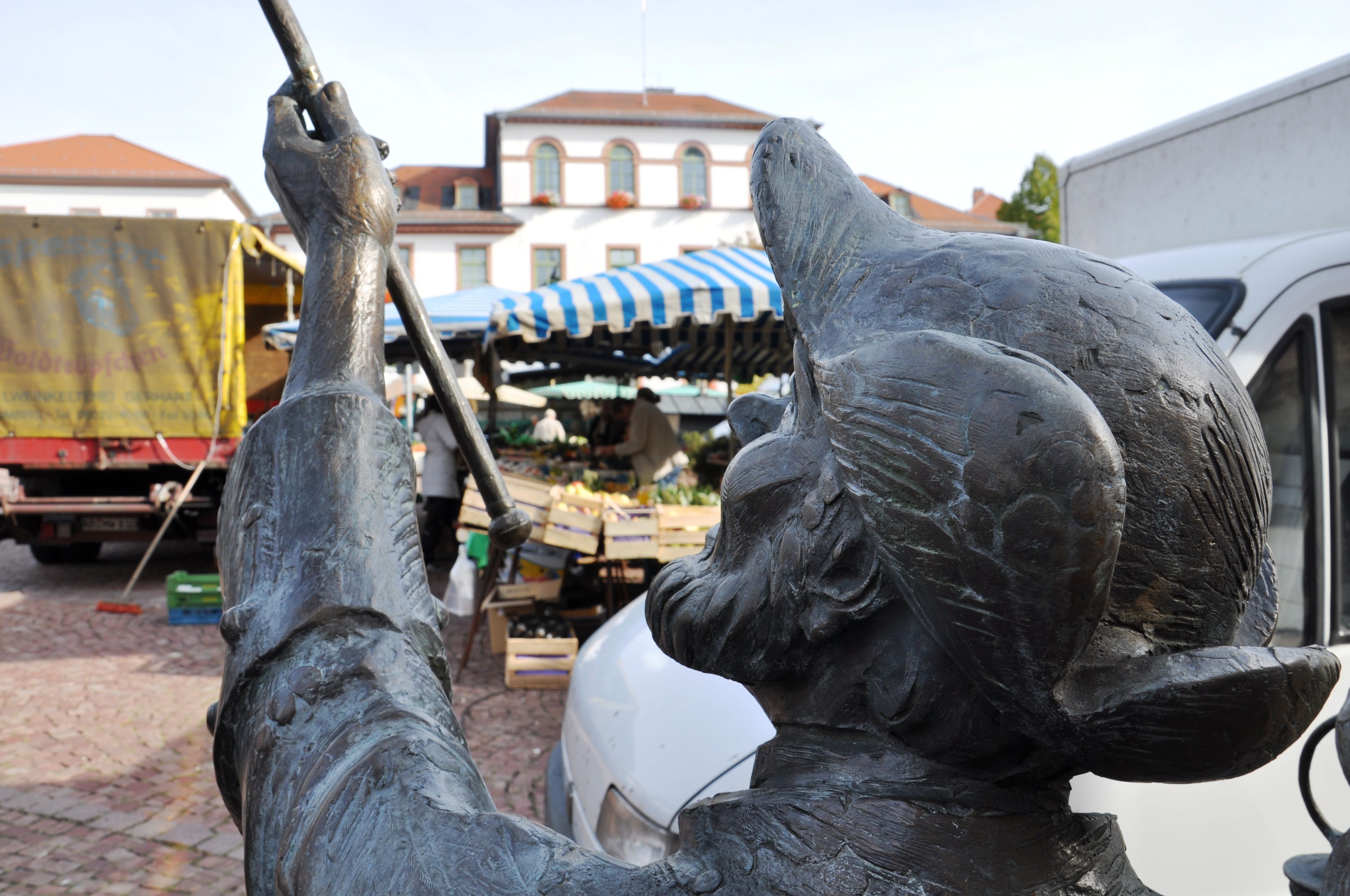 Die Bronzefigur Nachtwächter vor der Kulisse des Wochenmarktes. 