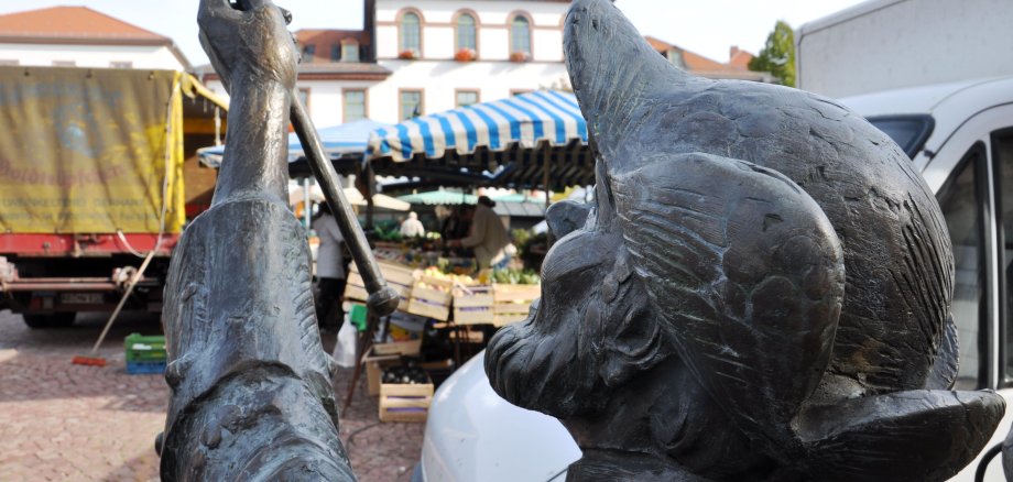 Die Bronzefigur Nachtwächter vor der Kulisse des Wochenmarktes. 